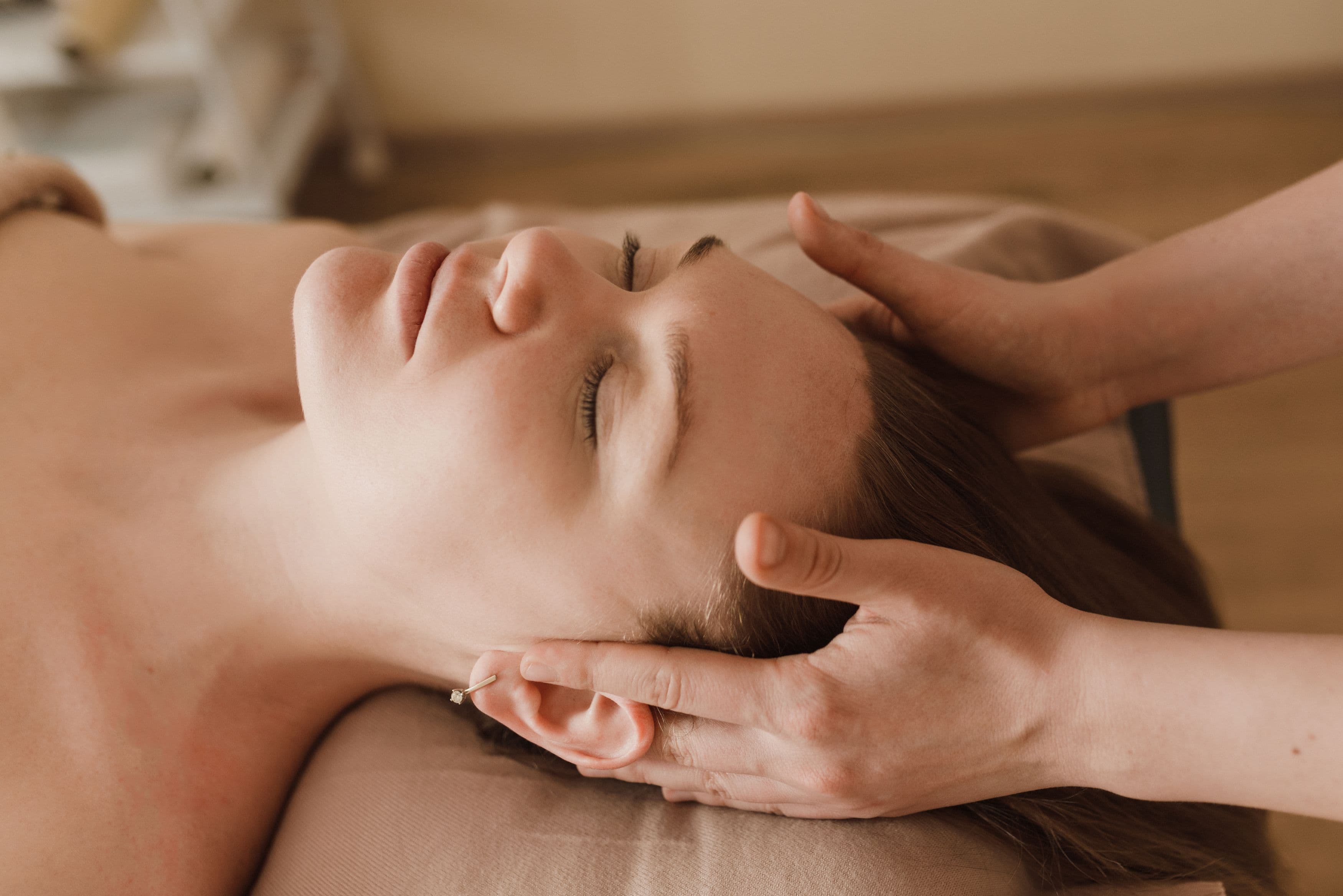 Massage relaxant de la tête et du visage pour une femme aux yeux clos.