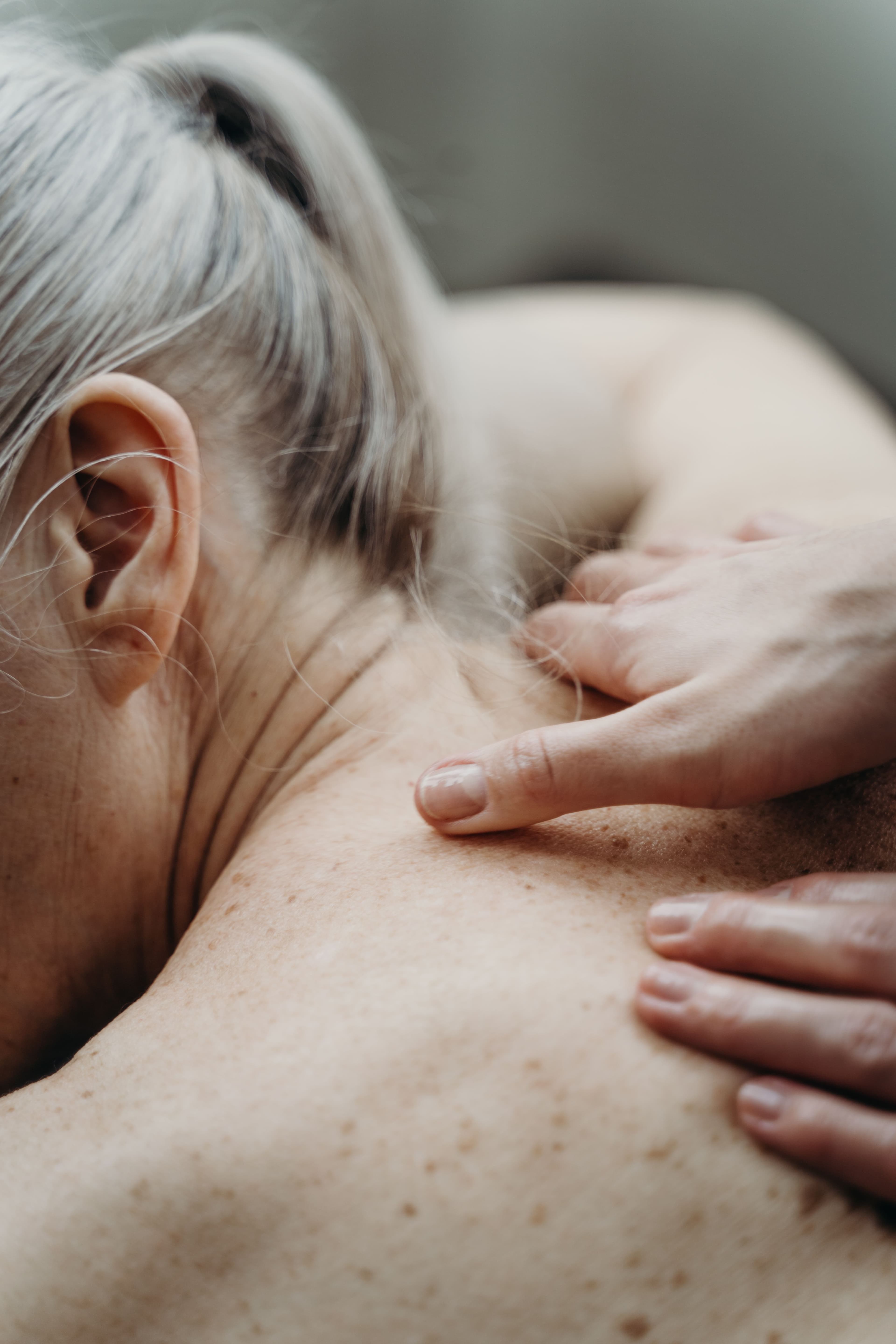 Mains massant le haut du dos et le cou d'une femme âgée aux cheveux gris.
