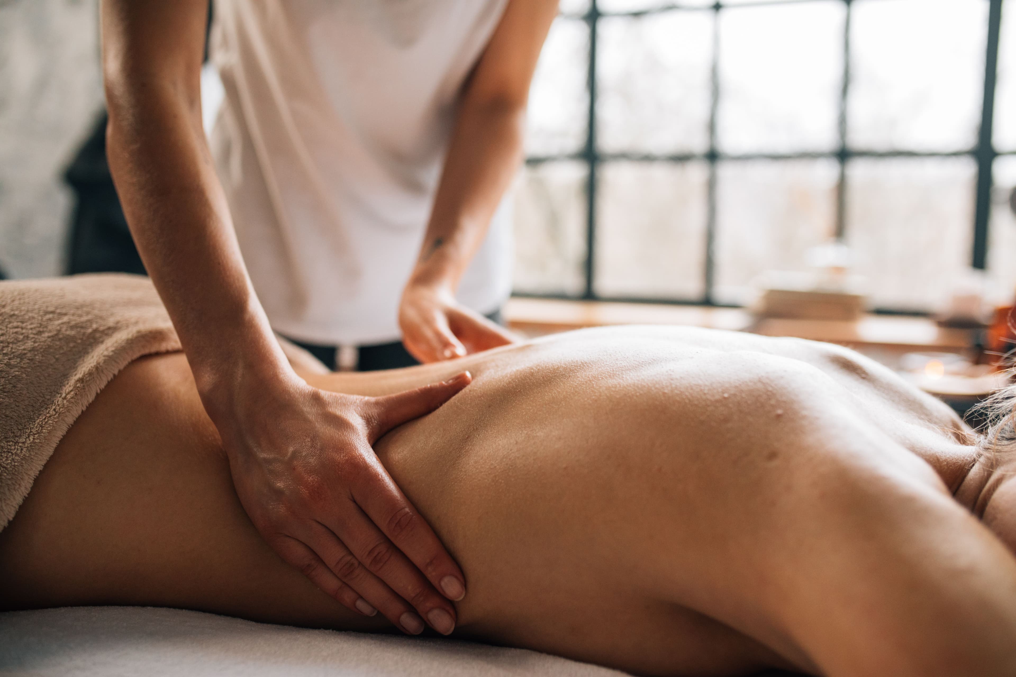 Mains d'une thérapeute massant le dos d'une personne allongée dans un salon de bien-être.
