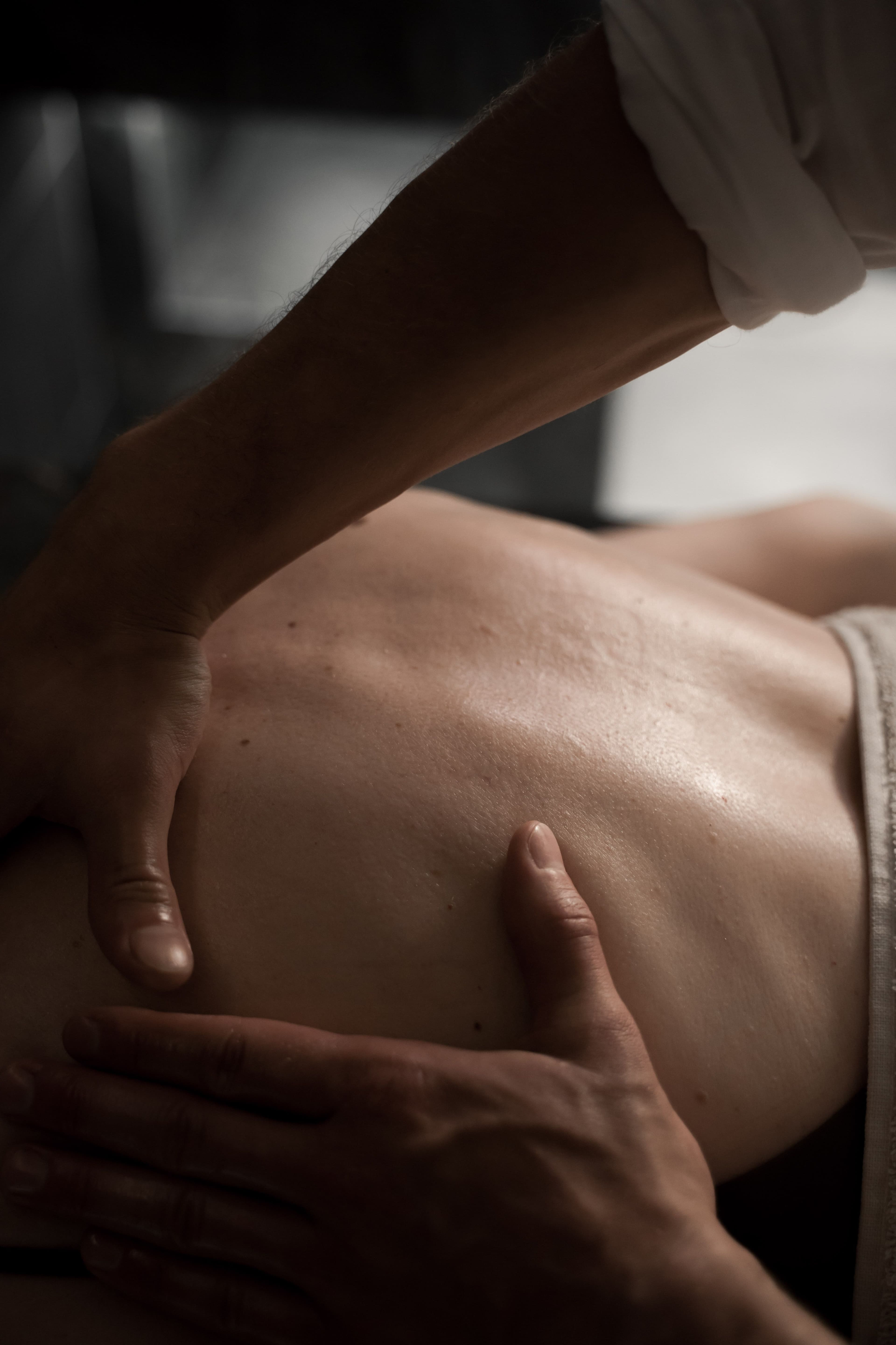 Mains massant fermement le dos nu d'une personne sous un éclairage doux et dramatique.